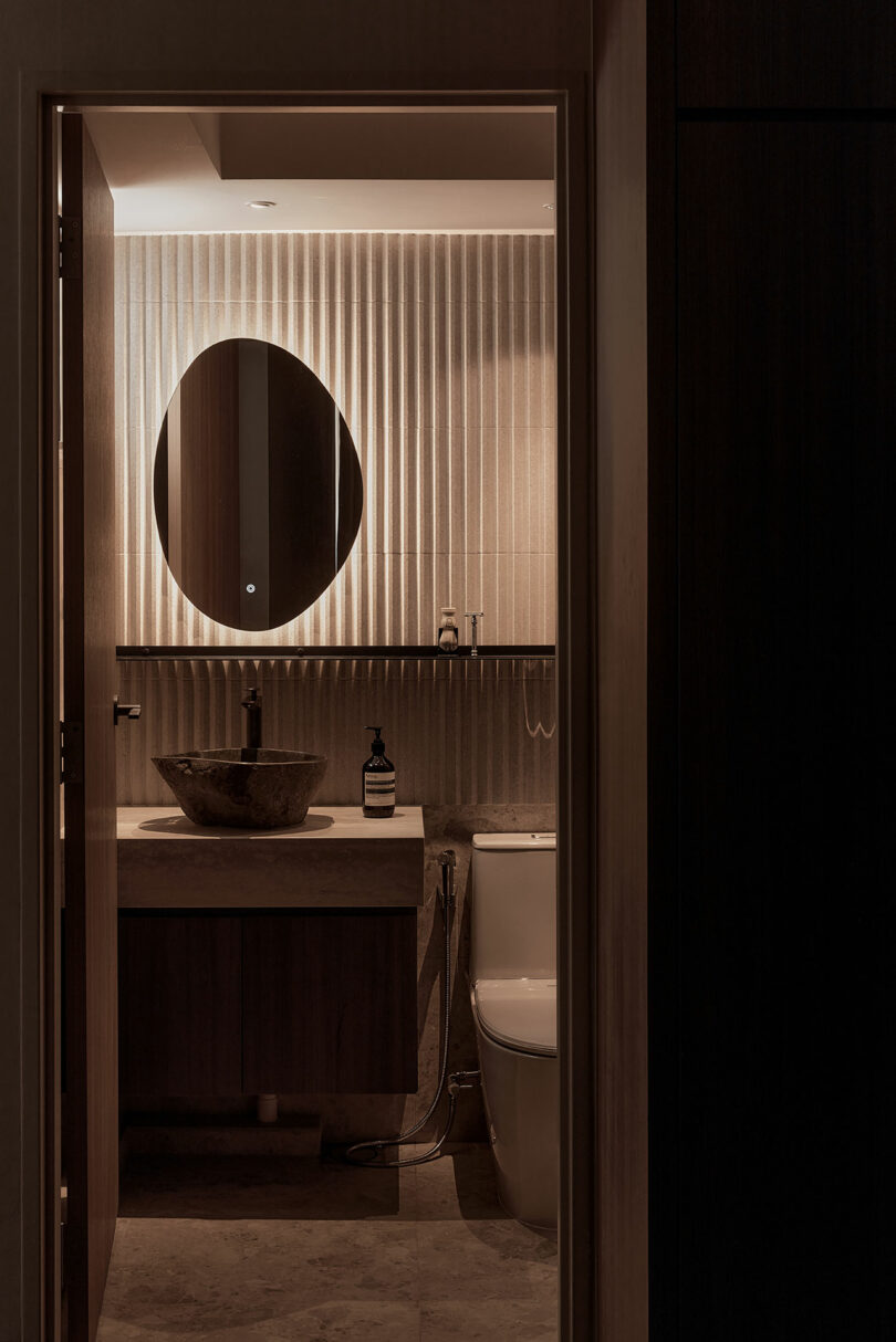 view into dark modern bathroom with back-lit mirror