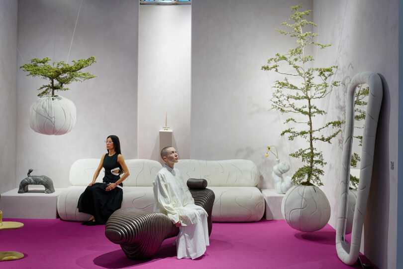Two people, the designers, sitting with their exhibition of contemporary, sculptural furnishings.