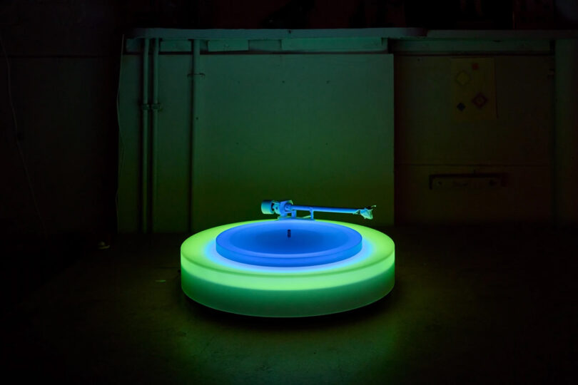Brian Eno's Turntable II on a table glowing green and blue in a green light illuminated room.