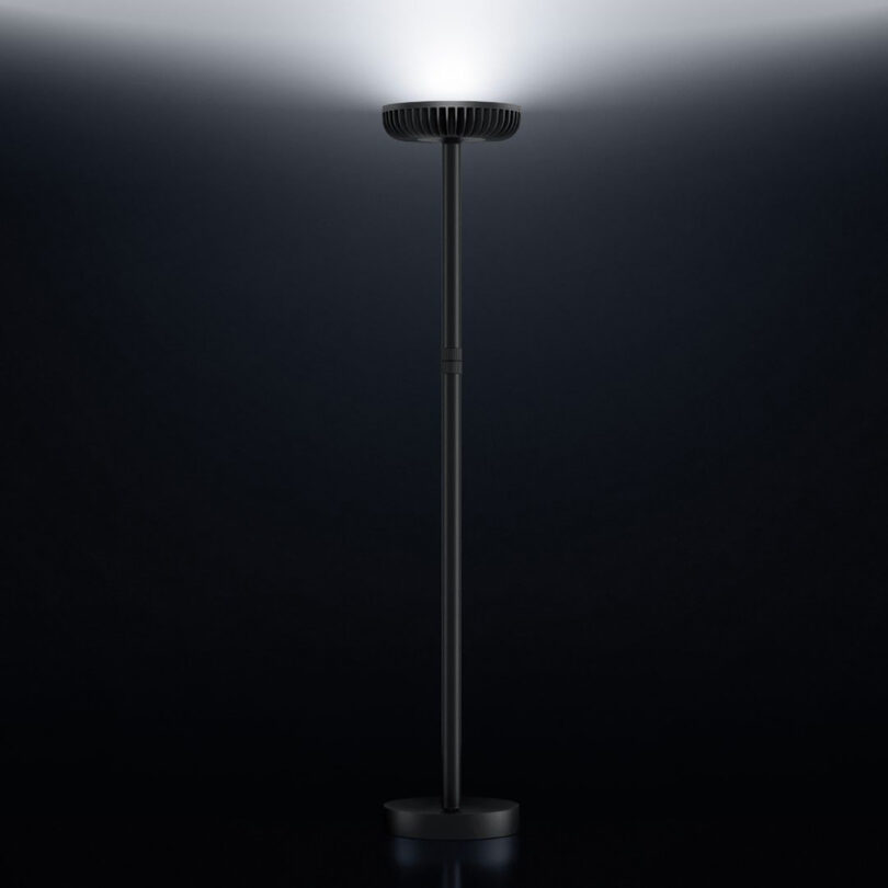 Full front view of Brighter floor lamp with its circular LED array glowing upward in a dark room.