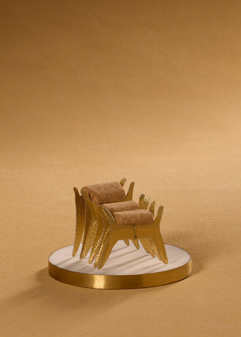 A miniature chair made from champagne bottle packaging presented on a tiny plinth.