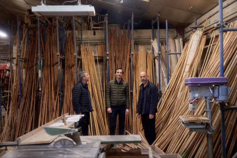 three men standing in a workshop lined with walls of caning