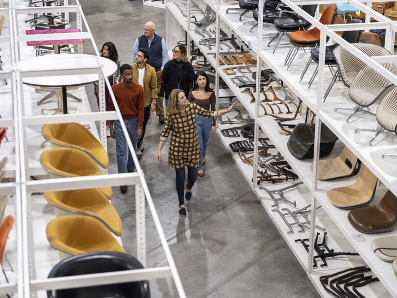 Llisa Demetrios, chief curator and granddaughter of Ray and Charles Eames, leading a small group of visitors through two rows of Eames designed chairs within the new Eames Archives in Richmond, California