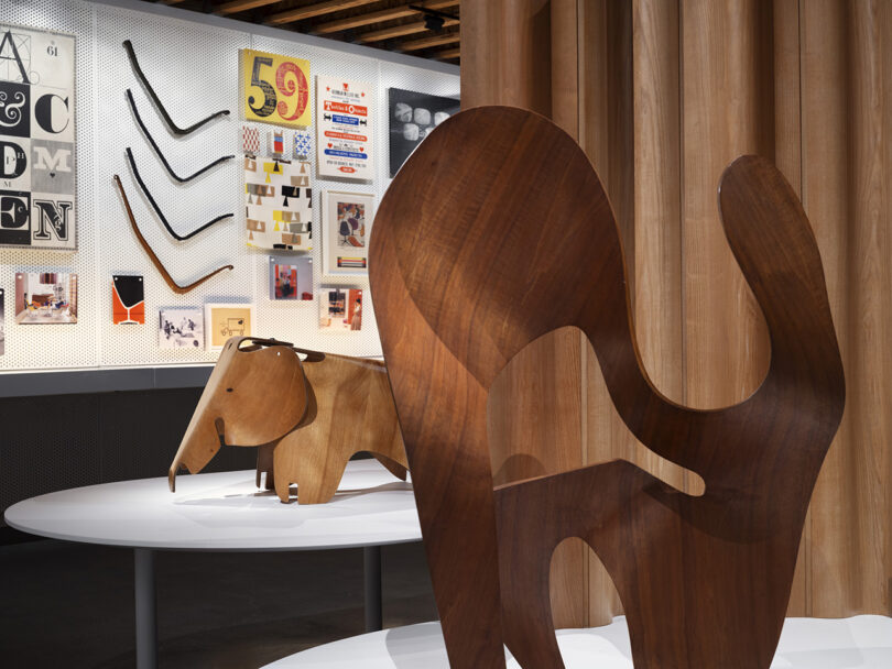 Two wooden sculptural pieces on display on platforms, one shaped like an elephant and the other abstract in design; both part of 40,000 artifacts including prototypes, products, tools, ephemera, and personal items owned and loved by Ray and Charles.