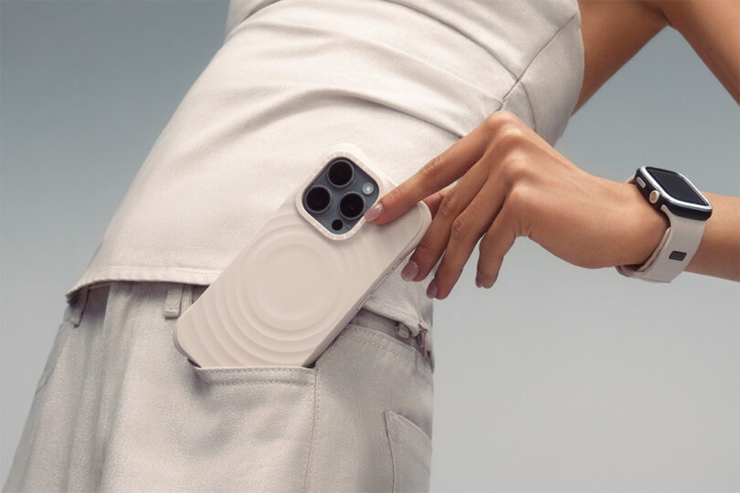 Woman's torso wearing Apple Watch, stone colored crop top, and pants pulling out an Oat Essentials by CASETiFY Ripple case from her pocket while leaning backwards.