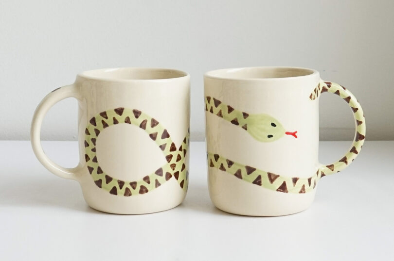 two side-by-side mugs with a snake painted on each