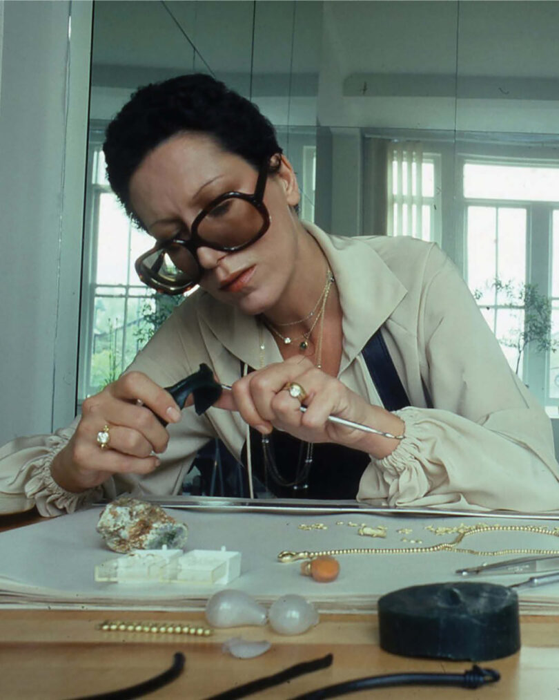 woman with dark hair and big glasses works with jewelry on a table