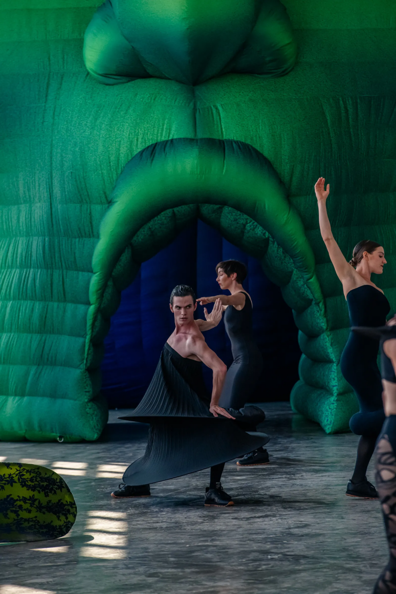 modern dancers in front of a large inflated emerald green face with an open mouth