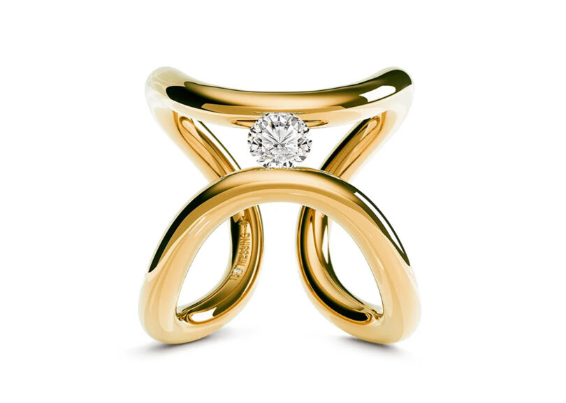 Curved gold ring with a hanging diamond on a white background