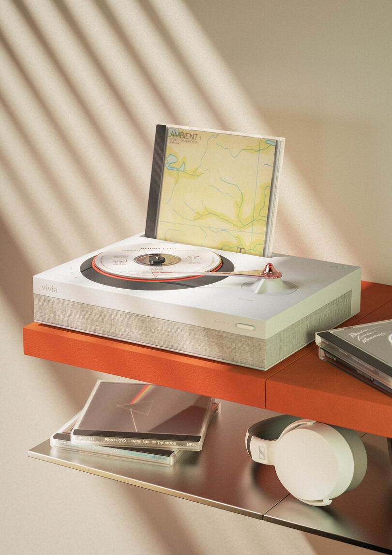 Vivia turntable for compact discs set on an orange floating shelf with a Brian Eno compact disc on display and on the player's platter. Underneath on a second level shelf are more CDs and a pair of white headphones.