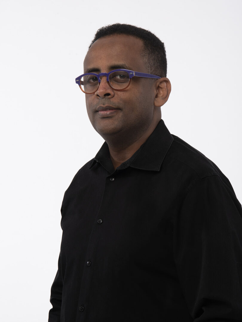 brown-skinned man with short black hair wearing glasses and a black button down shirt