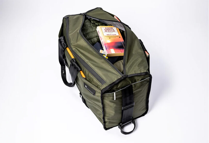 Mission Workshop Mass Transit duffel in Olive opened to reveal contents of clothing and a paperback book inside.