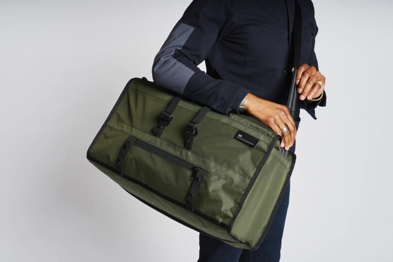 Man in jeans with olive Mission Workshop Mass Transit duffel slung across the shoulder using an optional sling strap.