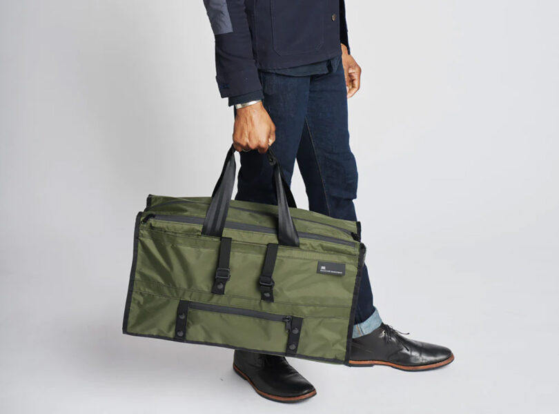 Man in jeans holding olive Mission Workshop Mass Transit duffel in right hand