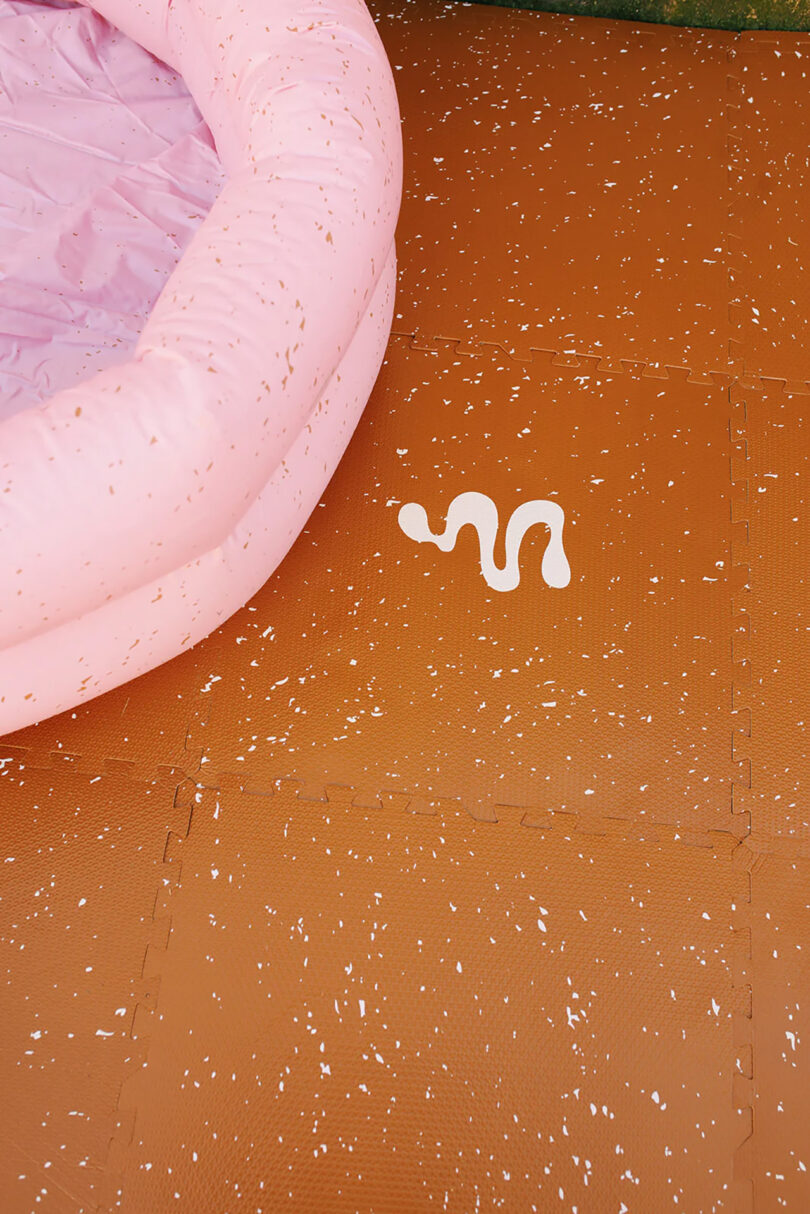Earthen hued 72" x 72" puzzle interlocking foam floor mat assembled and displayed alongside pink Mylle inflatable pool on top.