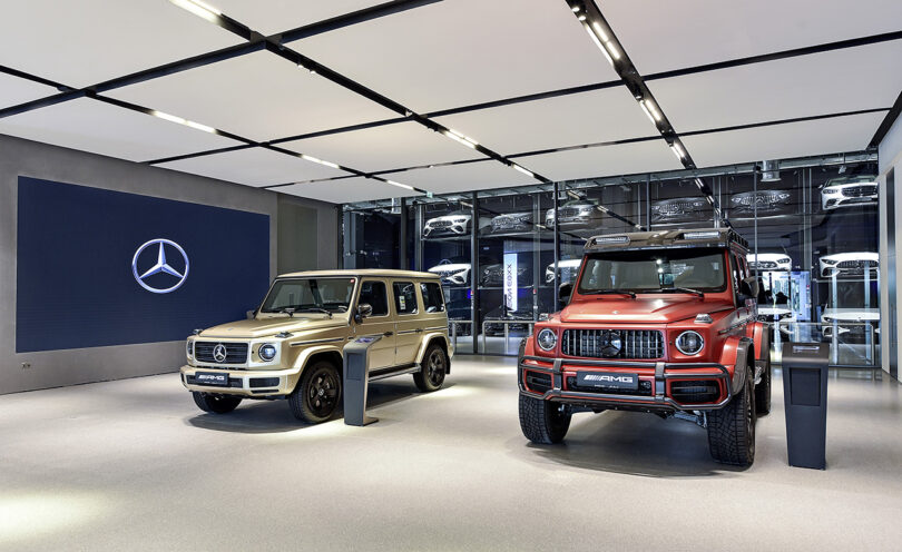 Центр бренда Mercedes-Benz в интерьере выставочного зала Дубая с двумя внедорожниками AMG, припаркованными перед большим экраном.