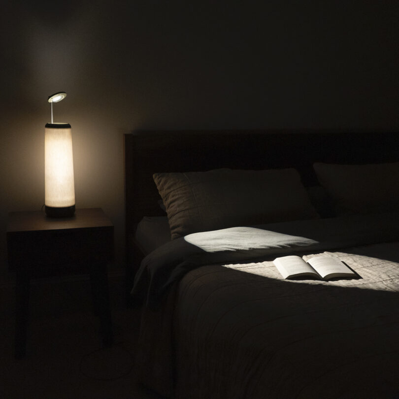 bedside table on a nightstand shining onto a book on a bed