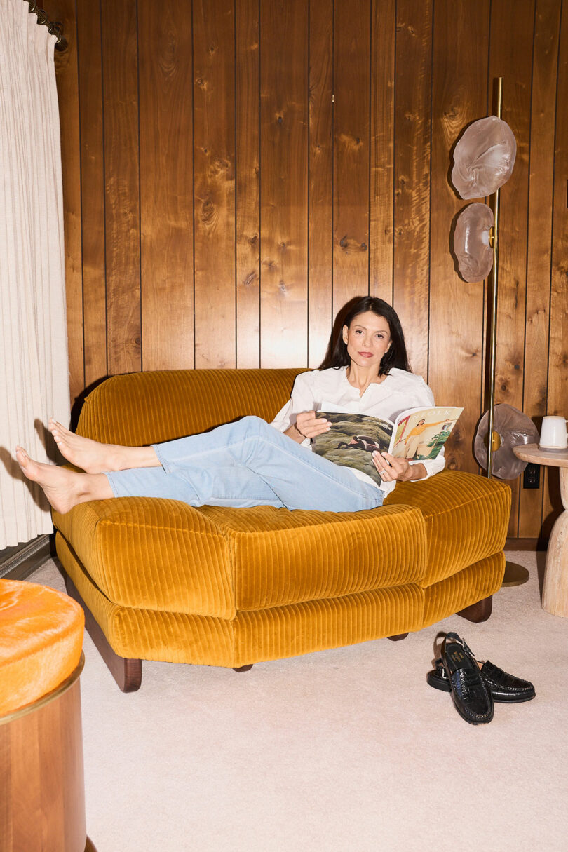 Woman reading a magazine in an oversized corduroy lounge chair in a wood paneled room.