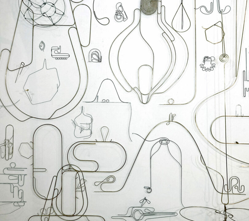 Wire sculptures hanging on a white studio wall.