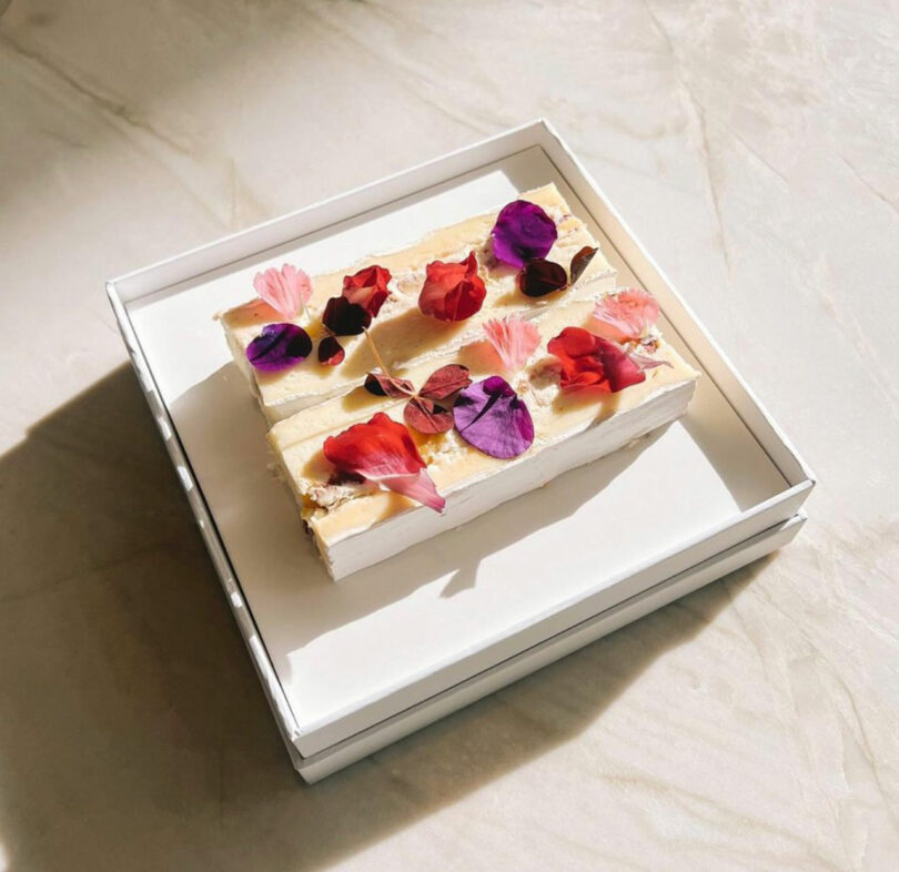angled down view of square white plate holding artfully arranged cheese with flowers on top