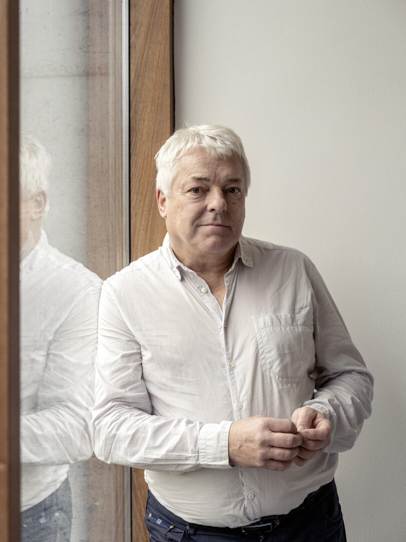 light-skinned man with short white hair wearing a white button down shirt