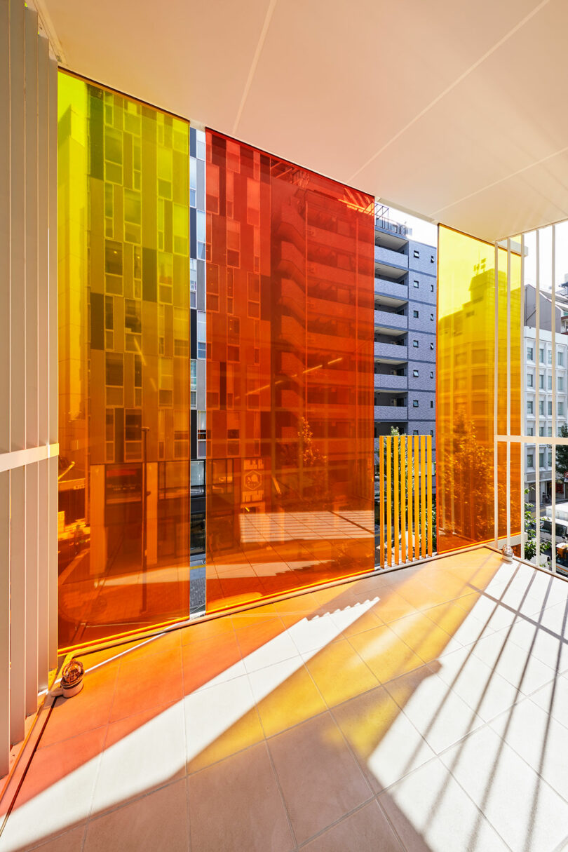 نمای داخلی زاویه دار فضای اداری مدرن که به بالکن با شیشه های بیرونی نارنجی و زرد نگاه می کند