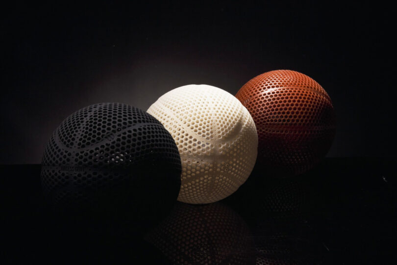 A trio of 3D printed Wilson Gen1 basketball in brown, black and white lined up diagonally against an all-black background.