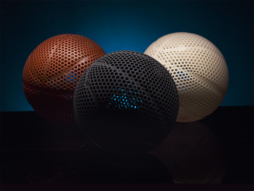 A trio of 3D printed Wilson Gen1 basketball in brown, black and white set against an all-black background with subtle blue glow behind the three.