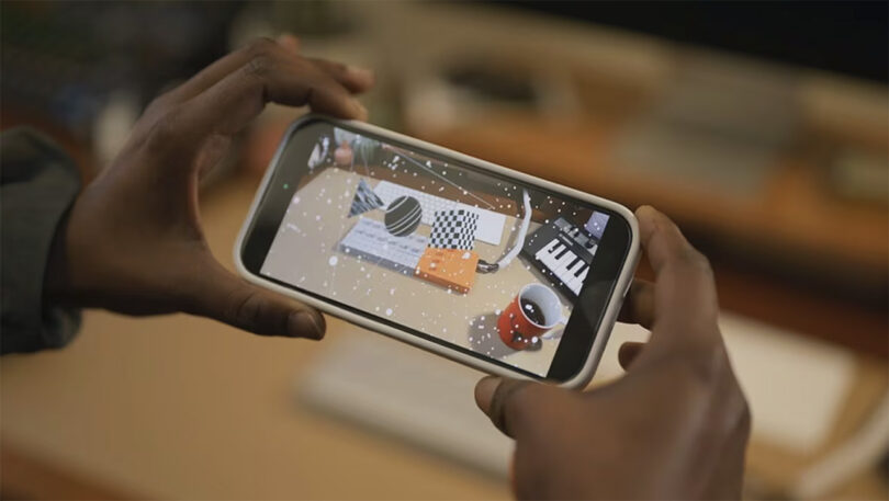 Person holding iPhone in landscape mode using Yamaha SEQTRAK music creation station augmented reality app feature, looking at the SEQTRAK with virtual design patterns overlayed across the screen.