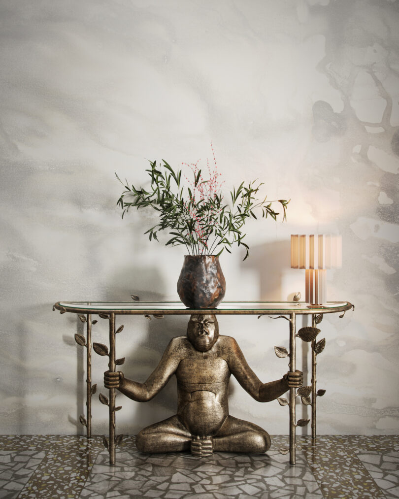 sculptural console table with a vase of flowers and lamp on top in wallpapered room