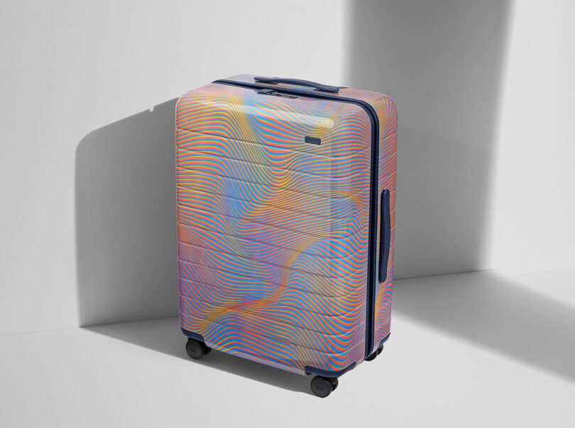 A colorful, patterned luggage with four wheels stands against a white backdrop with a prominent shadow to its left.