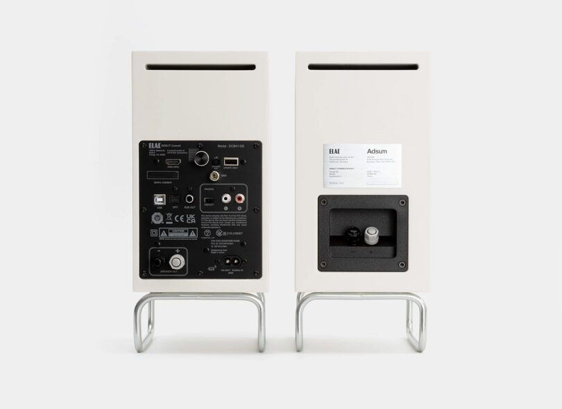 Two Adsum + ELAC Debut CONNEX DCB41 audio speakers with their back panels port connections displayed on stands against a white background.