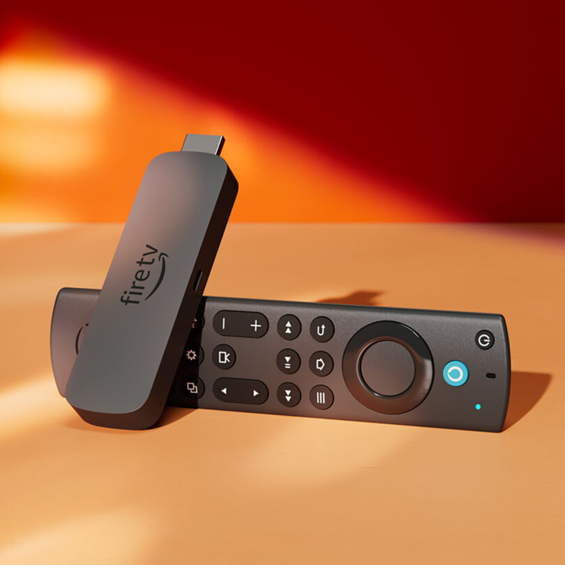 An Amazon Fire TV remote is sitting on top of a table with an orange and red background.