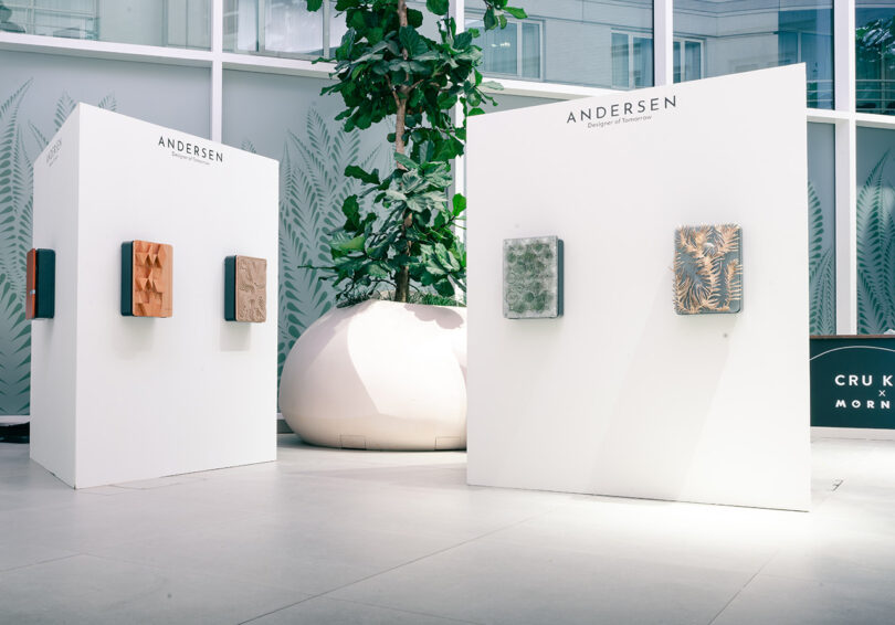 Gallery display with five framed student concepts on free-standing panels in a modern atrium setting featuring Andersen EV chargers.