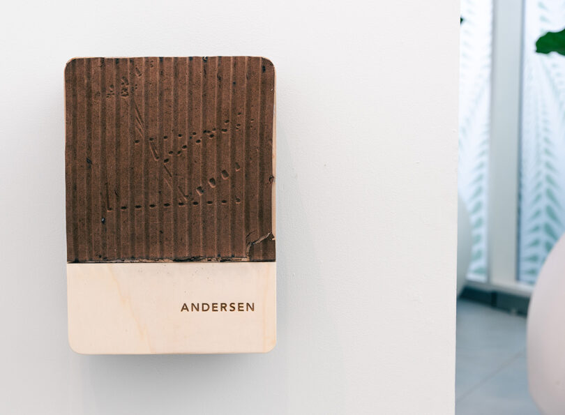 A fluted wall mounted dual-tone Andersen EV charger made from recycled coffee grounds, displayed on a white wall.