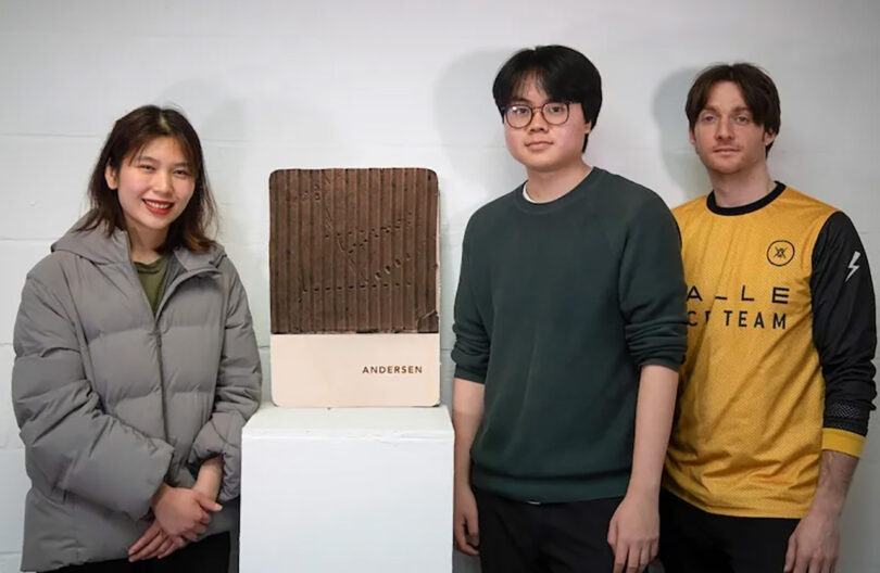 Three students from the University of Creative Arts standing beside their winning design labeled "Java", an Andersen EV Charger with a fluted panel from recycled coffee grounds.