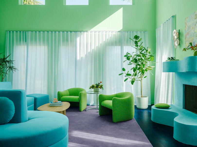 اتاق نشیمن پر جنب و جوش با شومینه آبی، مبلمان سبز، دیوارهای سبز روشن، و پرده های شفاف.