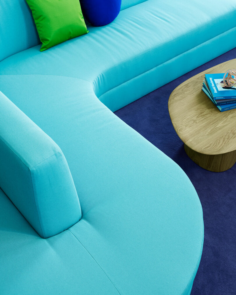 Vibrant blue sofa with bright accent pillows paired with a round wooden coffee table in a modern living space.