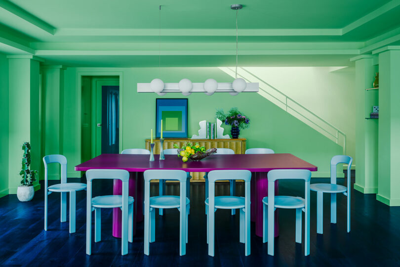 اتاق غذاخوری معاصر پر جنب و جوش با میز بنفش، صندلی‌های آبی روشن، و دیوارهای سبز.