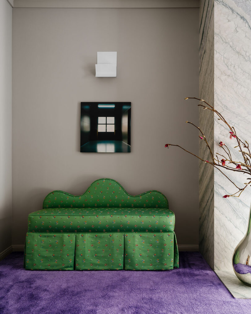اتاقی امروزی با مبل طرح‌دار سبز روی دیوار خاکستری، با نقاشی کوچک بالای آن، فرش‌های بنفش تیره و گلدان روی زمین