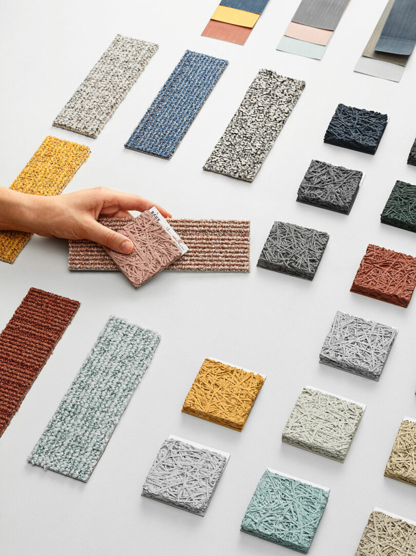 Colorful carpet samples and wall tile displayed on the floor in a clean, white industrial space.