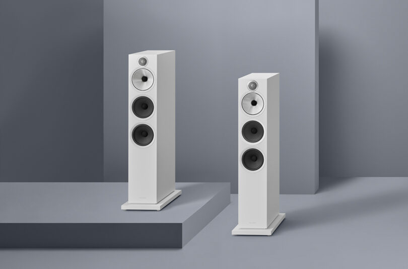 Two white Bowers & Wilkins 600 Series floor-standing speakers in a minimalist gray room.