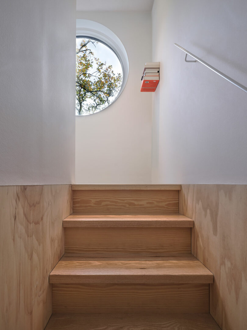 A wooden staircase leading to a window in a small house.