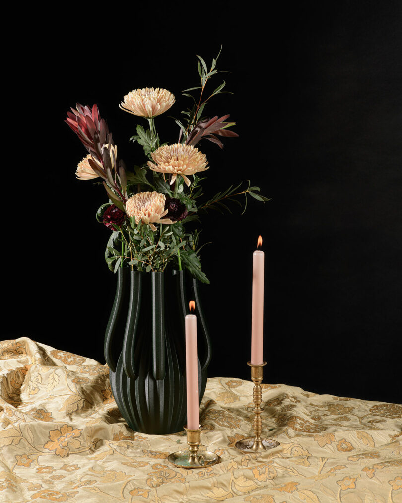 A contemporary vase with flowers on the table placed behind two candles.