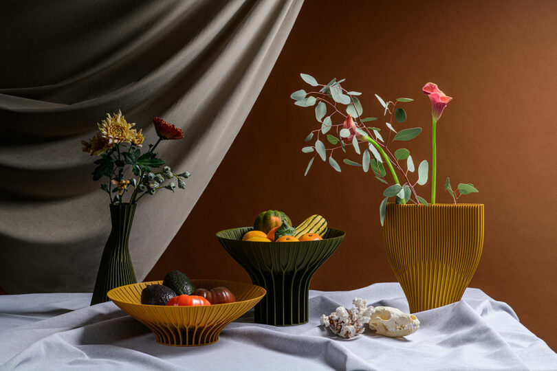 Several textures vases with flowers and bowls with fruits on a table scape.