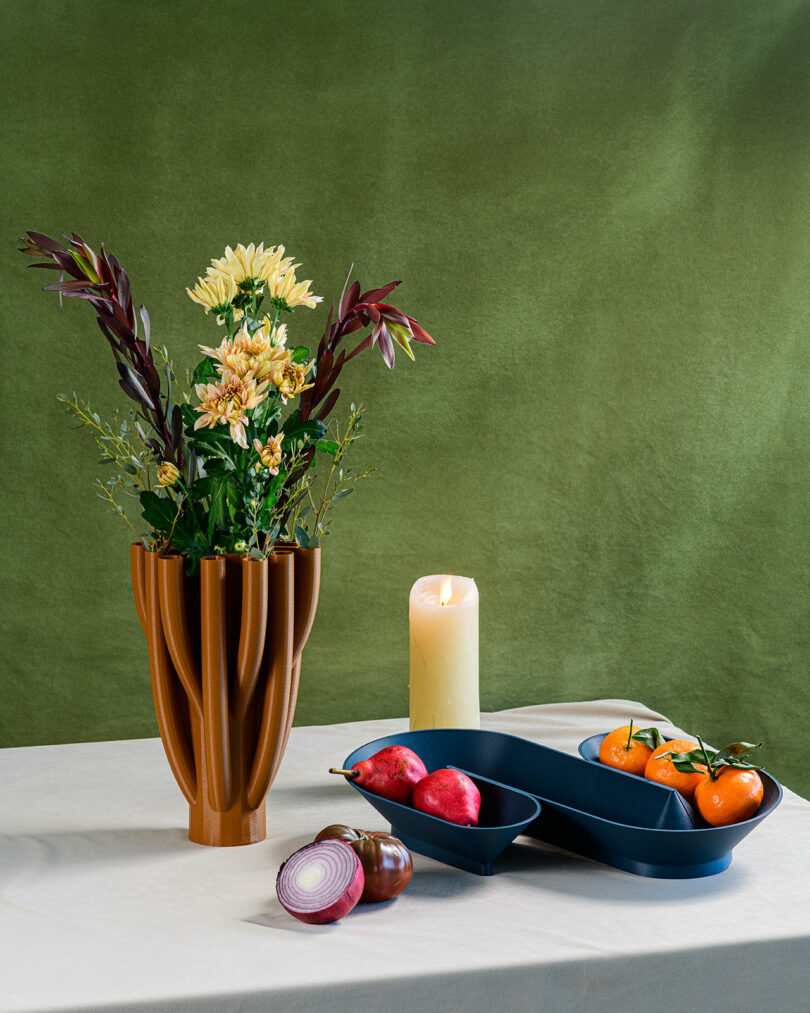A textured vase with flowers and a winding bowl with fruits on a table scape.