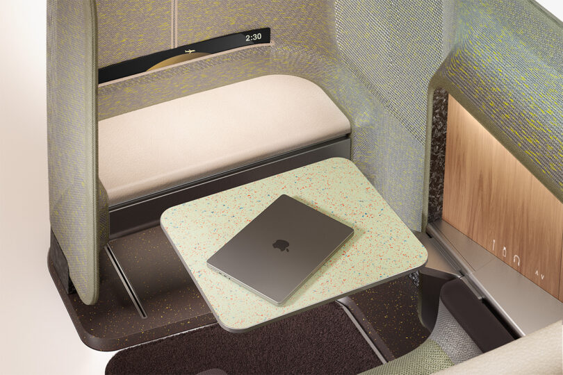 A modern airplane cabin interior with a single aircraft seat design and a foldable table featuring a closed laptop.
