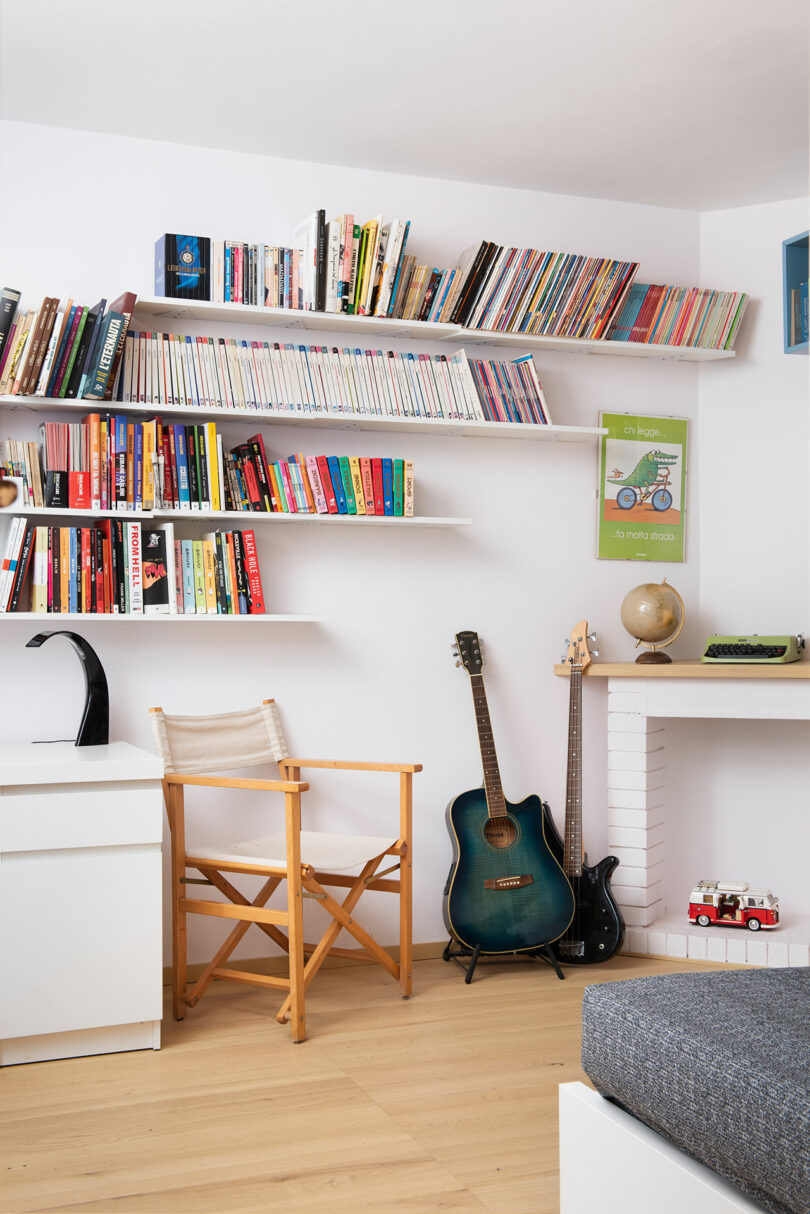 angled view into bedroom with white shelves holding books and a guitar leaning against wall