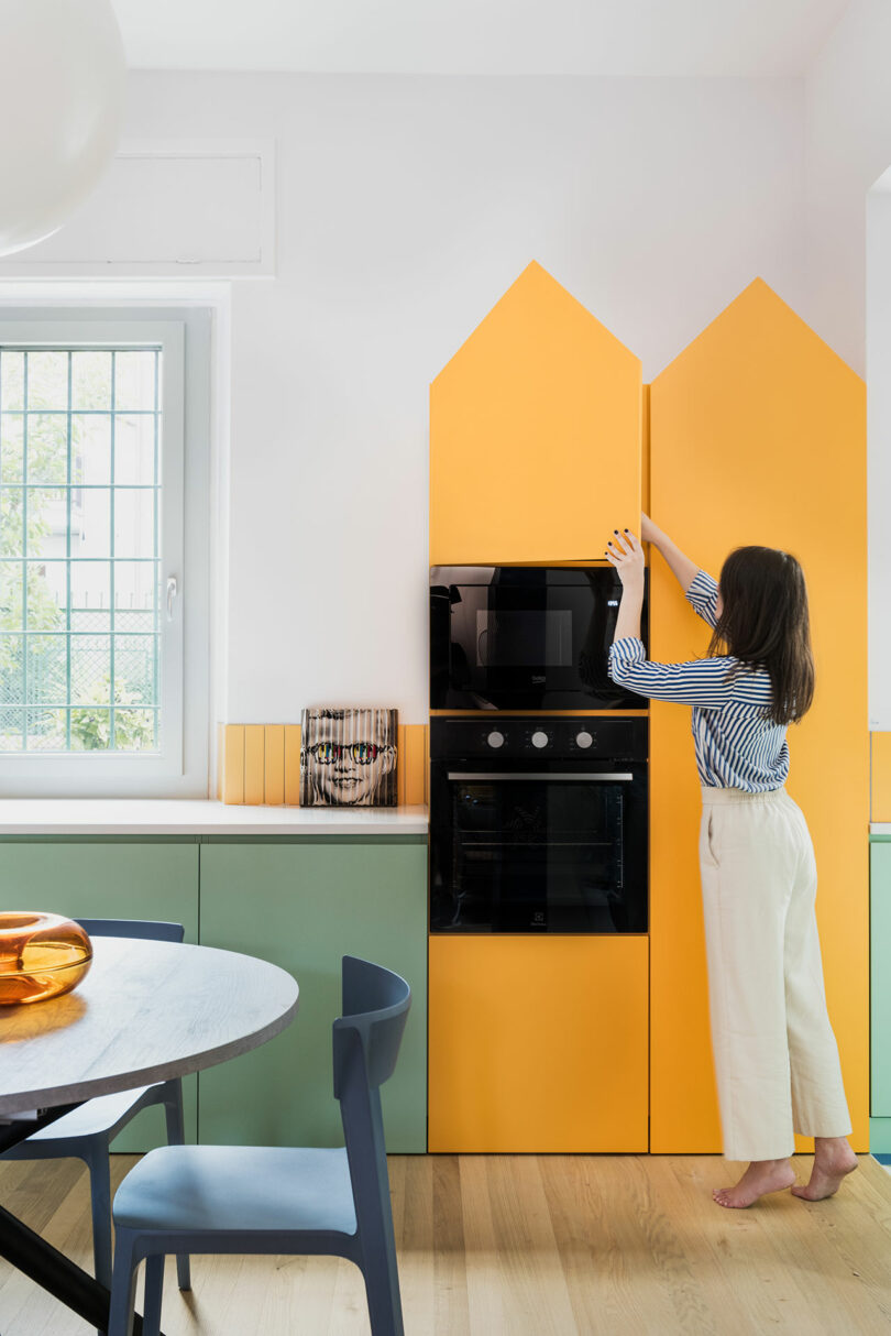 A woman is standing in a kitchen with colorful cabinets.