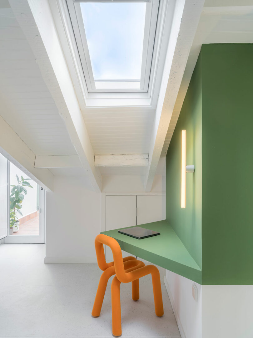Minimalist attic study with skylights, a green desk area, and an orange chair.